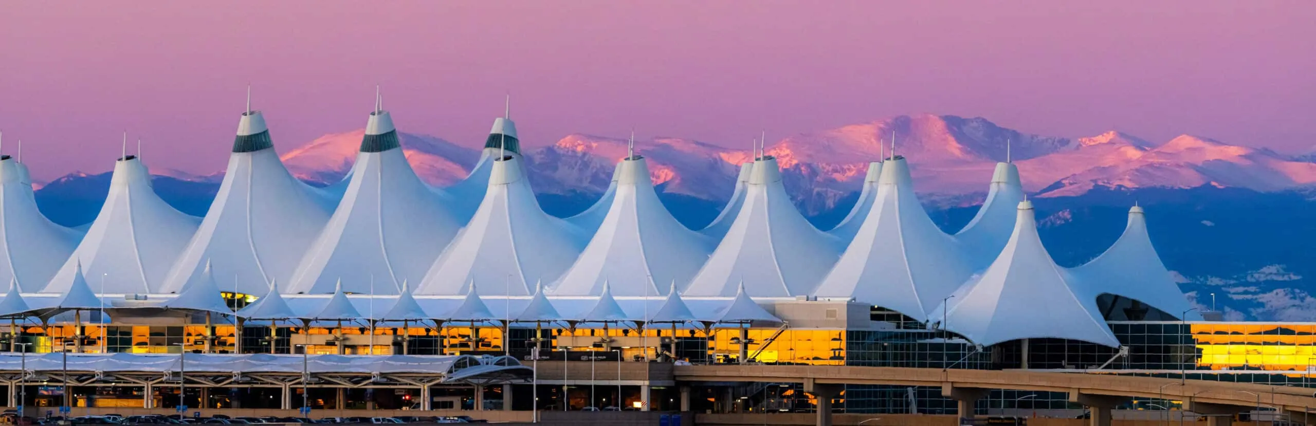 The iconic white peaked roof of Denver International Airport at sunset, a primary destination for our Denver airport car service.